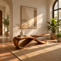 Low ribbon bench with a looping base and a long flat top in a bright entryway with arched windows and plants