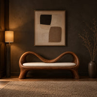 Bench with a wave shaped ribbon frame and a slim pale seat pad in a dark entryway at golden hour