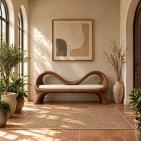 Bench with a wave shaped ribbon frame and a slim pale seat pad in a bright entryway with arched windows and plants