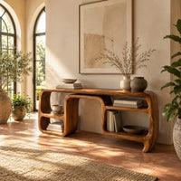 Console table with looping ribbon sides and open cubbies on both ends in a bright entryway with arched windows and plants
