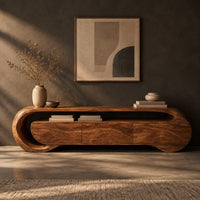 Corner detail of wooden tv stand with a looping ribbon band and wave carved front panels beside wood, brass and linen samples