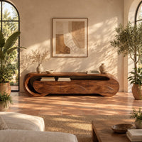 Wooden tv stand with a looping ribbon band and wave carved front panels in a bright living room with arched windows and plants