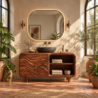 Bathroom vanity with ripple carved doors, open shelves and short tapered feet in a bright bathroom with arched windows and plants