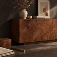 Corner detail of four door sideboard carved with concentric ripple rings on a plinth base beside wood, brass and linen samples