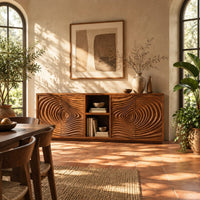 Sideboard with four ripple carved doors and two open shelves in the middle in a bright dining room with arched windows and plants