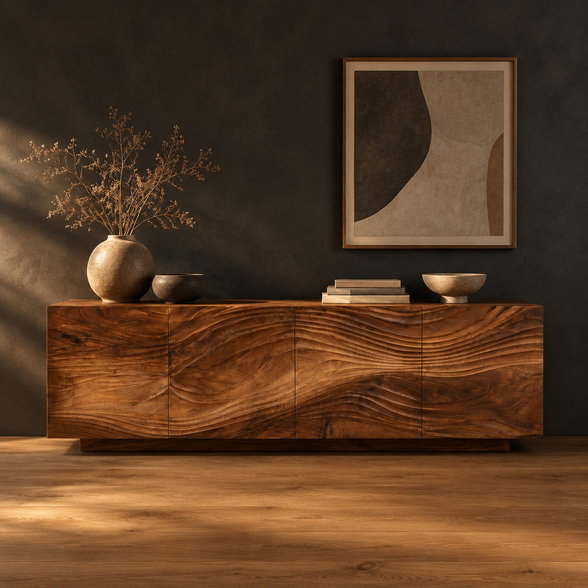 Low sideboard with four carved wave panels on a recessed plinth base in a dark studio against a charcoal plaster wall