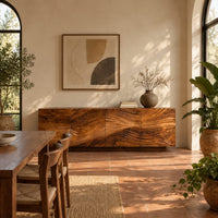 Low sideboard with four carved wave panels on a recessed plinth base in a bright dining room with arched windows and plants