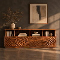 Corner detail of tv stand with ripple carved front panels and four open display shelves beside wood, brass and linen samples
