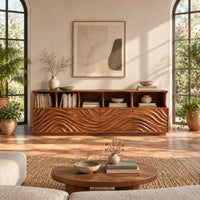 Tv stand with ripple carved front panels and four open display shelves in a bright living room with arched windows and plants
