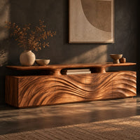 Corner detail of low wooden tv stand with wave carved doors and a raised top shelf beside wood, brass and linen samples