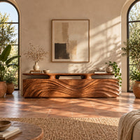 Low wooden tv stand with wave carved doors and a raised top shelf in a bright living room with arched windows and plants