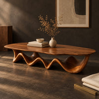 Corner detail of long coffee table with a freeform oval top on a rippling wave shaped base beside wood, brass and linen samples