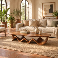 Long coffee table with a freeform oval top on a rippling wave shaped base in a bright living room with arched windows and plants