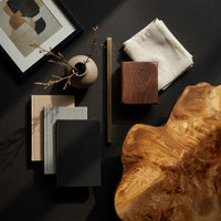 Corner detail of free form live edge low table on stump legs beside wood, brass and linen samples