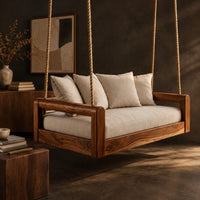 Corner detail of rope hung swing with open frame arms and a deep seat cushion beside wood, brass and linen samples