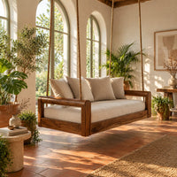 Rope hung swing with open frame arms and a deep seat cushion in a bright porch with arched windows and plants