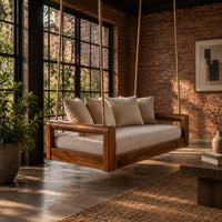 Rope hung swing with open frame arms and a deep seat cushion in an industrial loft porch with exposed brick