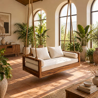 Wooden swing hung from four thick ropes with a low solid wood frame in a bright porch with arched windows and plants