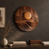 Detail of round wall art with a raised sun over layered carved waves beside wood, brass and linen samples