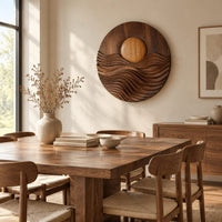 Round wall art with a raised sun over layered carved waves beside a dining table in natural light