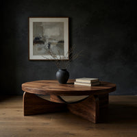 Round coffee table on a crossed plank base in a dark studio against a charcoal wall