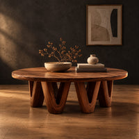 Round coffee table with a wide flat top on chunky v shaped legs in a dark studio against a charcoal plaster wall