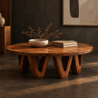 Corner detail of round coffee table with a wide flat top on chunky v shaped legs beside wood, brass and linen samples