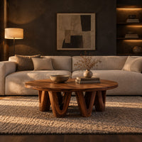 Round coffee table with a wide flat top on chunky v shaped legs in a dark living room at golden hour