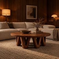 Round coffee table with a wide flat top on chunky v shaped legs in an evening living room with walnut wall paneling