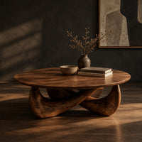 Round coffee table with a thin top and a crossed sculpted base, three-quarter view showing the grain