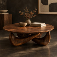 Corner detail of round coffee table with a thin top and a crossed sculpted base beside wood, brass and linen samples
