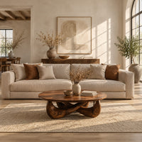 Round coffee table with a thin top and a crossed sculpted base in a bright open plan living room
