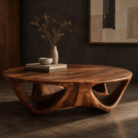 Corner detail of round coffee table with a flared sculpted base and scooped arch openings beside wood, brass and linen samples