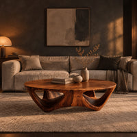 Round coffee table with a flared sculpted base and scooped arch openings in a dark living room at golden hour