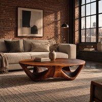 Round coffee table with a flared sculpted base and scooped arch openings in an industrial loft living room with exposed brick