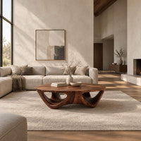 Round coffee table with a flared sculpted base and scooped arch openings in a bright open plan living room