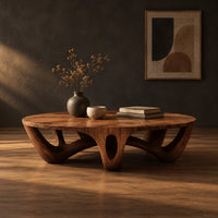 Round coffee table with arched sculpted legs and oval openings in a dark studio against a charcoal plaster wall