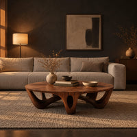 Round coffee table with arched sculpted legs and oval openings in a dark living room at golden hour
