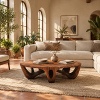 Round coffee table with arched sculpted legs and oval openings in a bright living room with arched windows and plants