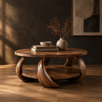 Round coffee table with crescent shaped legs and a round lower shelf in a dark studio against a charcoal plaster wall