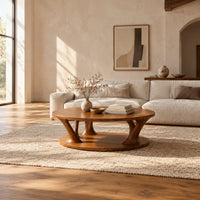 Circular coffee table with flared legs standing on a low base disc in a bright open plan living room