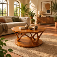 Circular coffee table with forked antler shaped legs above a wide disc base in a bright living room with arched windows and plants