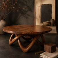 Corner detail of round coffee table with a thick top and an interlaced looping wood base beside wood, brass and linen samples