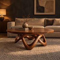 Round coffee table with a thick top and an interlaced looping wood base in a dark living room at golden hour
