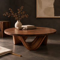 Corner detail of round coffee table with a low swooping arch base beside wood, brass and linen samples