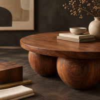 Corner detail of round coffee table with a thick top resting on three large wooden balls beside wood, brass and linen samples