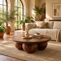 Round coffee table with a thick top resting on three large wooden balls in a bright living room with arched windows and plants