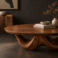 Corner detail of round coffee table with a thick top on a sculpted base with two arches beside wood, brass and linen samples