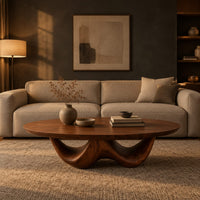 Round coffee table with a thick top on a sculpted base with two arches in a dark living room at golden hour