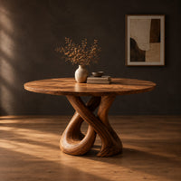 Round dining table on a sculpted base of two crossing wooden loops in a dark studio against a charcoal plaster wall